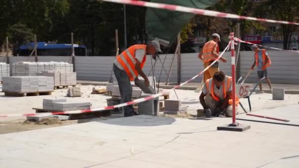 Oekraïne, Mariupol - 1 september 2020. Construstiewerkers leggen stenen plavuizen op het nieuwe stadsplein. Bouwers repareren stoeptegels met troffel, hamer om vlakke vlakke vlakke ondergrond te maken. — Stockvideo