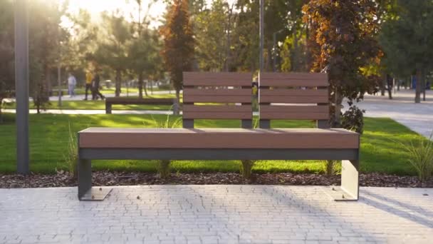 Moderní dřevěné lavičky na trávníku v parku. Stylová nová lavička v rekreační oblasti města při východu nebo západu slunce. Urbanismus téma veřejného prostoru krajiny design. Žádní lidé na prázdném chodníku. — Stock video