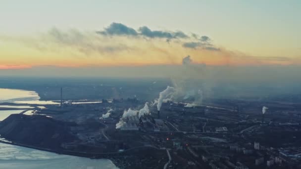 Metallurgische fabriek aan de kust van de winterzee. Bovenaanzicht van de fabriek, rook stijgt uit de schoorstenen. Industrieel centrum aan de rand van de stad in de avond bij zonsondergang — Stockvideo