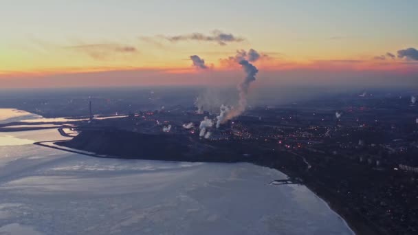 Hutní závod na pobřeží zimního moře. Horní pohled na továrnu, kouř stoupající z komínů. Průmyslové centrum na okraji města večer při západu slunce — Stock video