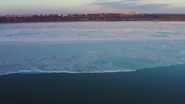 Retirada de la costa con un pequeño pueblo al atardecer. estructura cambiante de hielo marino, derretimiento de hielo con la distancia de la costa. Calentamiento de primavera en el mar. Ciudad costera en una noche de invierno. Vista aérea. — Vídeos de Stock