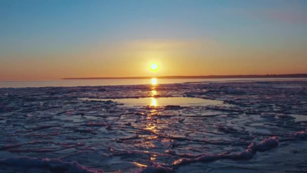 Vista aerea del tramonto sul mare ghiacciato d'inverno. Il drone vola verso l'alba e l'orizzonte. Il volo dell'elicottero sopra la deriva di ghiaccio che si scioglie verso il sole. Riscaldamento primaverile. Vivido cielo colorato. — Video Stock