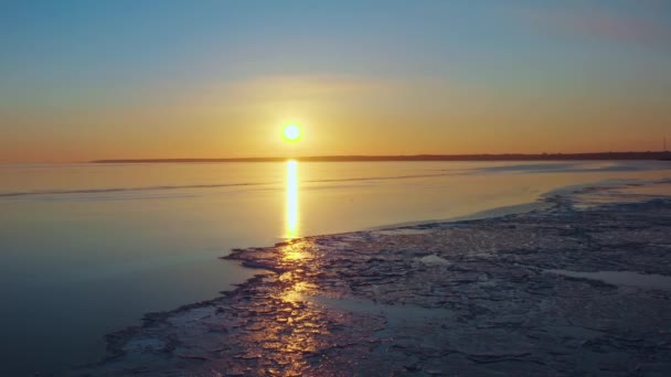 Zonsondergang over de bevroren zee, ondergaande zon vanaf de kustlijn, luchtvlucht over het smeltende ijs Lente opwarming over de zee Kleuren van de lucht en de zee bij zonsondergang in de winter. Drone-beelden. — Stockvideo