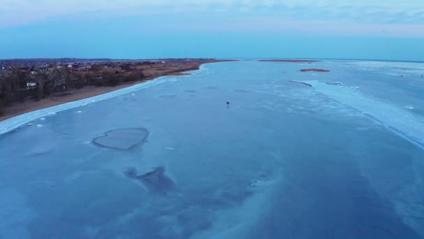Ein Mann läuft bei Sonnenuntergang auf dem Eis des gefrorenen Meeres nahe der Küste der Stadt Schlittschuh. Eislauftraining. Winterfreizeit am Meer. Drohnenaufnahmen. — Stockvideo