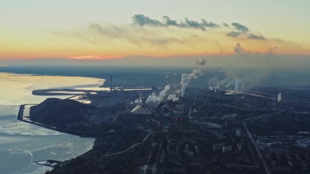 Metallurgische fabriek aan de kust van de winterzee. Bovenaanzicht van de fabriek, rook stijgt uit de schoorstenen. Industrieel centrum aan de rand van de stad in de avond bij zonsondergang — Stockvideo