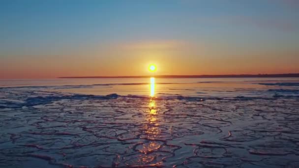 氷結した海の上の日没、海岸線からの太陽の沈む夕日、溶融氷の上の航空便海の上の春の温暖化冬の日没で空と海の色。ドローン映像. — ストック動画