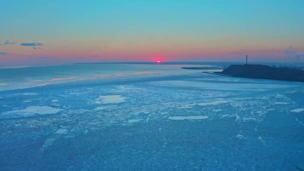 Luchtfoto van zonsondergang boven de bevroren winterzee. Drone daalt af boven de oceaan bij zonsopgang. Vlucht over smeltend ijs en industrieel stadsbeeld. Het broeikaseffect. Levendige kleurrijke lucht. Industriële installaties. — Stockvideo