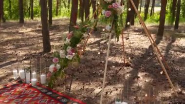 Pembe güllerle süslenmiş tahta çubuklardan yapılmış bohem çadır kemeri, halıdaki mumlar, pampass otları, çam ormanlarındaki açık hava düğün mekanında peri ışıklarına sarılmış. Çiçeksel kompozisyonlar.