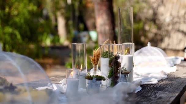 Γαμήλια δεξίωση έξω στο δάσος. Τραπεζαρία διακοσμημένη σε boho στυλ με κεριά, λευκό πανί, λουλούδια, σερβίρεται με πιάτα, επιτραπέζια σκεύη, πιάτα, γεύματα, ποτήρια και ποτά. Εστίαση διακοπών. — Αρχείο Βίντεο