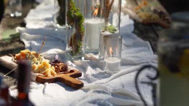 Düğün partisi dışarıda ormanda ziyafet veriyor. Mum, beyaz kumaş, çiçek, tabak, sofra takımı, yemek takımı, yemek takımı, kadeh ve içeceklerle süslenmiş yemek masası. Tatil yemekleri..