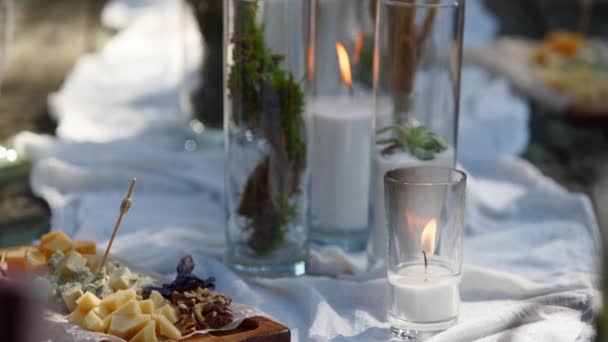 La persona toma queso de la mesa de comedor decorado en estilo boho con velas, tela, flores, servido con vajilla, platos, comidas, copas, bebidas. Banquete de boda catering al aire libre en el bosque. — Vídeos de Stock