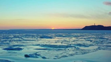 Donmuş kış denizi üzerinde gün batımının havadan görünüşü. İnsansız hava aracı gün doğumuna ve ufka doğru uçuyor. Eriyen buzun üzerinden helikopter uçuşu güneşe doğru sürükleniyor. Bahar ısınması. Canlı renkli gökyüzü.