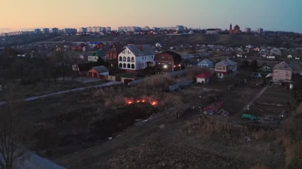 Βραδινή φωτιά σε ένα χωράφι κοντά στην πόλη. Καίει καλάμια κοντά σε σπίτια. Εποχιακές πυρκαγιές στην περιοχή της στέπας. Στοιχείο πυρός ως συνέπεια αυθαίρετων πυρκαγιών. Βίντεο με drone. — Αρχείο Βίντεο