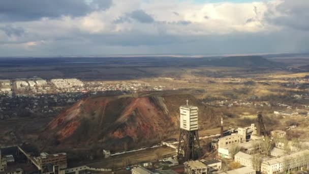 Old coal mine elevator and slag heaps on a cloudy day. Vintage coal mining shaft building, weathered factory and constructions. Fossil fuel and minerals mining heavy industry landscape with terrikons. — 图库视频影像