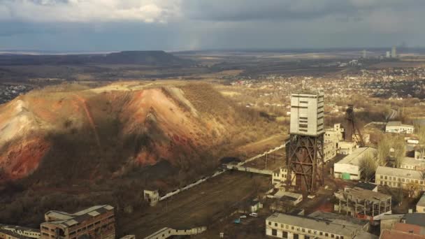 Old coal mine elevator and slag heaps on a cloudy day. Vintage coal mining shaft building, weathered factory and constructions. Fossil fuel and minerals mining heavy industry landscape with terrikons. — 图库视频影像