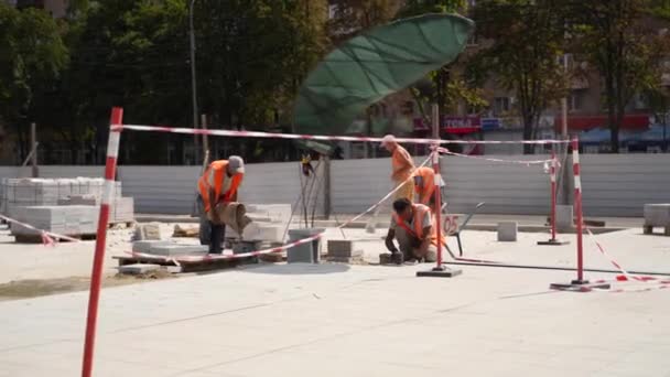 Ucrania, Mariupol - 1 de septiembre de 2020. Trabajadores de la construsción colocando losas de pavimentación de piedra en la nueva plaza de la ciudad. Constructores reparación de baldosas de colocación de acera con paleta, mazo para hacer la superficie plana nivelada. — Vídeos de Stock
