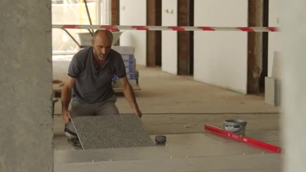 Ukraine, Mariupol - September 1, 2020. Worker lays the white ceramic tile on the floor. Professional tiler levels the porcelain stoneware flooring hitting with mallet on construction site. — Vídeo de Stock