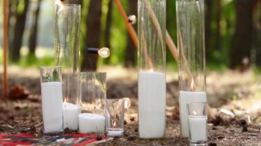 Camdan vazolarda yanan mumlar, bohem kemerinin yanındaki halının üzerinde şişeler güllerle süslenmiş ve çam ormanındaki açık hava düğün mekanında çiçeklere sarılmış çiçekler. Boho rustik dekor.