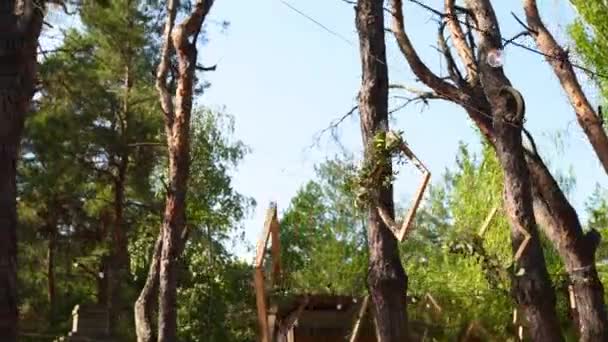 Banquete de boda al aire libre en un bosque de pinos. Mesas de comedor, bancos decorados en estilo boho con velas, flores, luces de hadas primaverales, platos, gafas de vino, marcos de madera. Decoración floral ecológica. — Vídeos de Stock