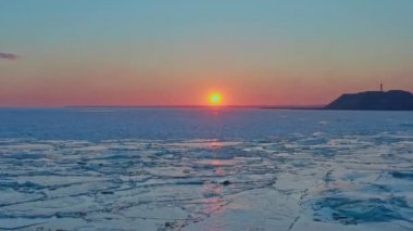 Donmuş kış denizi üzerinde gün batımının havadan görünüşü. İnsansız hava aracı gün doğumuna ve ufka doğru uçuyor. Eriyen buzun üzerinden helikopter uçuşu güneşe doğru sürükleniyor. Bahar ısınması. Canlı renkli gökyüzü.