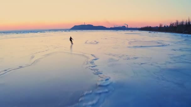 Mies luistelee jäätyneellä merellä lähellä teollisuuskaupungin rannikkoa auringonlaskun aikaan. Luistelukoulutusta. Talvivapaa-aika meren rannalla. Lennokin kuvamateriaali. — kuvapankkivideo