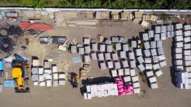 Aerial top view of an open storage yard with building materials. Outdoor construction site warehouse with machinery, cement, cables, bricks from above.