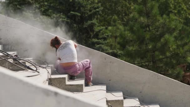 Ucrânia, Mariupol - 1 de setembro de 2020. Forte mulher areias parede de concreto com moedor de ângulo criando nuvem de poeira no local de construção. Trabalhadora no respirador corta concreto. Precauções. — Vídeo de Stock