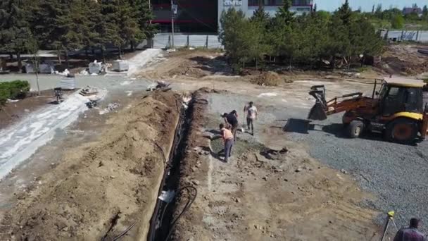 Ukraine, Mariupol - September 1, 2020. Workers digging trench on construction site. Loader tractor pours gravel of bucket. Underground channel with electric power cables. Infrastructure building. — Stok video