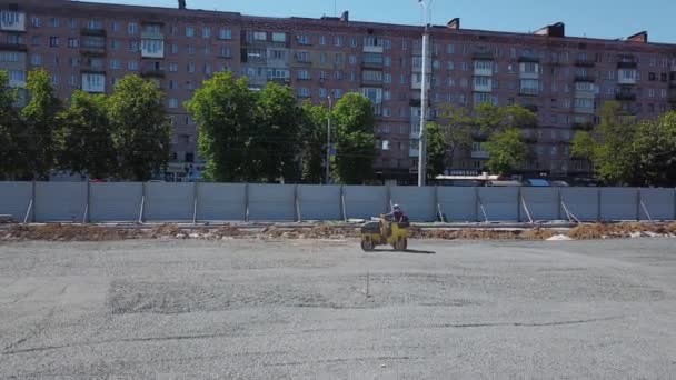 Ukraine, Mariupol - September 1, 2020. Road roller compacts gravel bed for paving slabs on new city square. Roller driver evens out the ground surface. Heavy equipment for earthwork. — Stock video