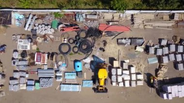 Aerial top view of an open storage yard with building materials. Outdoor construction site warehouse with machinery, cement, cables, bricks from above.