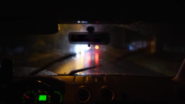 Pessoa dirigindo através de uma forte tempestade de chuva em uma cidade escura chuvosa. Luzes noturnas e chuva através do interior de um veículo enquanto uma pessoa dirige. Gotas de chuva no vidro. — Vídeo de Stock