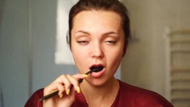 Young woman brushing her teeth looking in the mirror in bathroom. Pretty female doing a morning dental cleaning in bathroom. Girl cleans her mouth.