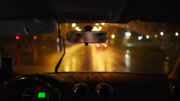 Homme traversant une forte tempête de pluie dans une ville sombre et pluvieuse. Des veilleuses et de la pluie traversent l'intérieur d'un véhicule pendant qu'une personne conduit. Gouttes de pluie sur le verre. — Video