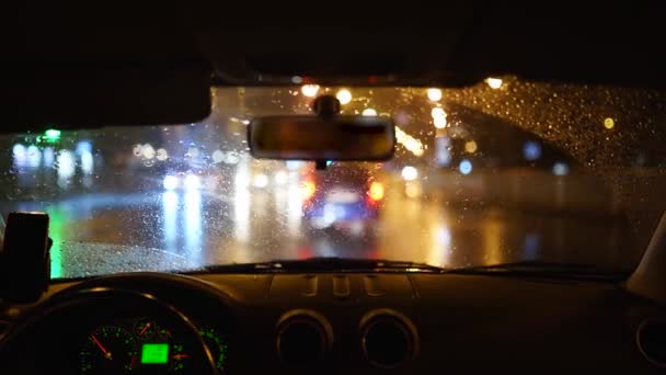 Man rijdt door een zware regenbui in een donkere regenachtige stad. Nachtlampjes en regen door het interieur van een voertuig terwijl een persoon rijdt. Regendruppels op het glas. — Stockvideo