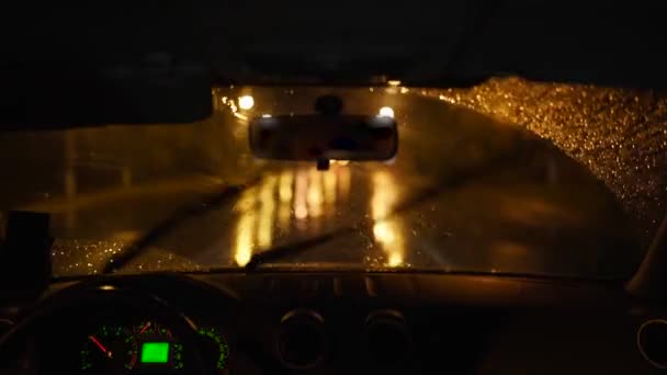 Человек, проезжающий через сильный дождь в темном дождливом городе. Ночные огни и дождь проходят через внутреннюю часть автомобиля, в то время как человек ведет машину. Капли дождя на стекле. — стоковое видео
