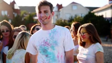 Yakışıklı adam renkli pudra tozuyla boyanmış göğsüne yumruklar yapıştırmış ve Holi festivalinde parmaklarıyla barış işareti göstermiş. Güzel kadınlar zıplar, dans eder. Hindu tatili. Kilitlemenin sonu, covid salgın, kısıtlamalar