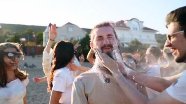 Neşeli adam başka bir adamın yanağına renkli pudra sıçratır ve sakalını sürer. Holi festivalinde ağır çekimde iyi eğlenceler. Hint bahar festivali, renkler, aşk. Covid salgın izolasyonunun sonu.