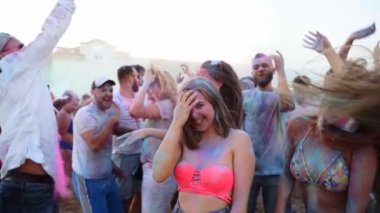 Zıplayan ve dans eden genç insanlar Holi festivalinde yavaş çekimde eğleniyor ve kuru renkler atıyorlar. Merkezdeki kız Hindu bayramını kutlamak için el çırpıyor. Salgının sonu