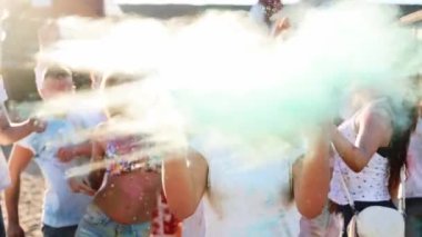 Hippi güneş gözlüklü güzel kız Holi festivalinde toz bulutu yaratmak için ellerini renkli tozla çırpıyor.