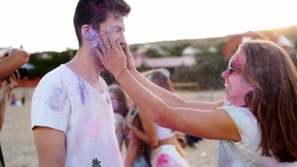 Femme souriante éclabousse et frotte la poudre bleu lavande sur les joues mans au festival Holi au ralenti. Couple s'amuse sur la plage pendant les vacances hindoues. Fin du confinement, pandémie de coqueluche, restrictions — Video