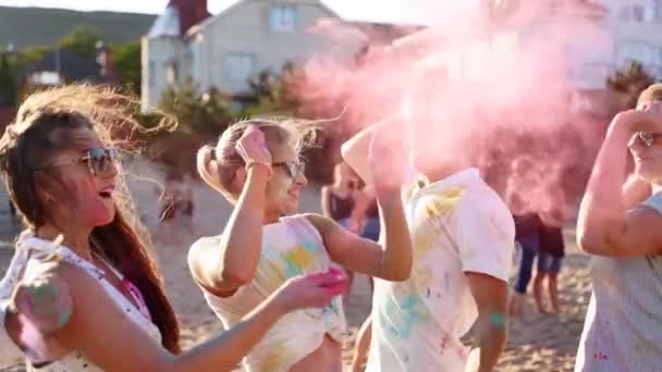 Cheerful people have fun, splash colored powder celebrating Holi festival on beach in slow motion. Friends dance, jump at hindu festival of spring, colours, love. End of covid pandemic isolation. — Stock Video