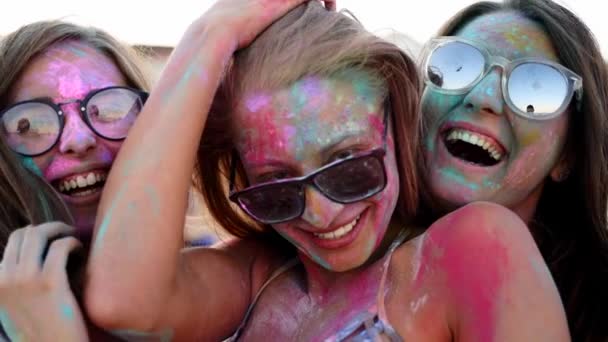 Trzy młode kobiety pokryte kolorowym, pudrowym uśmiechem, popisują się przed kamerą, bawią się na festiwalu Holi w zwolnionym tempie. Przyjaciele na plaży w hinduskich wakacjach. Koniec blokady, pandemia widealna — Wideo stockowe