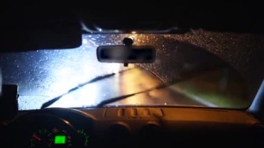 Karanlık yağmurlu bir şehirde sağanak yağmur altında araba kullanan biri. Bir insan araba kullanırken gece lambaları ve yağmurlar bir aracın içinde. Cama yağmur damlaları damlıyor.