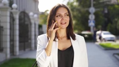 Genç akıllı bir kız akıllı bir telefonla yürüyor ve konuşuyor. Beyaz takım elbiseli bronzlaşmış güzel bir kız caddede yürüyor. Başarılı iş kadınları yemek molasında.