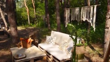 Loş kanepeli fotoğraf odası ve çam ormanlarındaki açık hava düğün mekanında boho stili kargo paletleri masası. Bohem dekor.