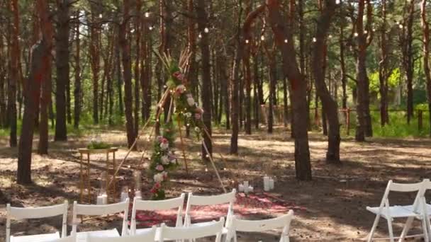 Krásné bohémské tipi obloukové dekorace na venkovní svatební obřad místo v borovém lese s kužely. Židle, květinové květinové kompozice růží, koberec, strunná vílí světla. Letní venkovská svatba. — Stock video