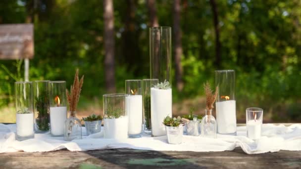 Banquet de mariage en plein air dans la forêt de pins. Tables de salle à manger décorées dans le style boho avec des bougies dans des vases en verre, tissu blanc, fleurs succulentes. Eco bio composition florale décor pour les vacances. — Video