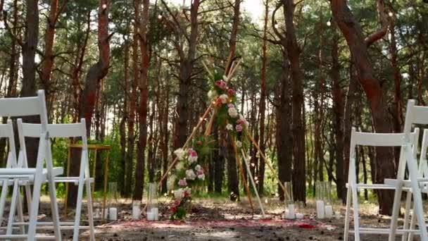 Красива богемська арка на відкритому місці весільної церемонії в сосновому лісі з конусами. Стільці, флористичні квіткові композиції з троянд, килима, струнні казкові вогні. Літнє сільське весілля . — стокове відео
