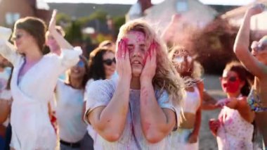 Güzel bir kadın yanaklarına renkli pudra sıçratır, gülümser, Holi festivalinde ağır çekimde eğlenir. İnsanlar Hindu bayramını ve koronavirüs salgınını, karantinayı, kısıtlamaları kutluyor..