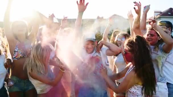 Young man surrounded by crowd gets splashes of colored powder onto belly by two women in slow motion. Friends have fun at hindu holiday of spring, colors, love. End of covid pandemic isolation. — Stock Video